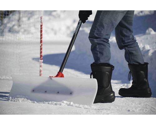 Person skottar snö med en snöskyffel på en isyta.