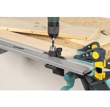 En borrmaskin med borrfixtur för pluggar borrar i en träplanka med Wolfcraft pluggklämmor.