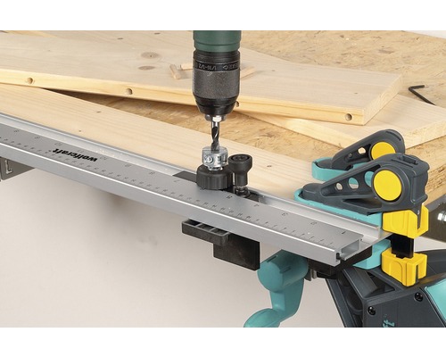 En borrmaskin med borrfixtur för pluggar borrar i en träplanka med Wolfcraft pluggklämmor.