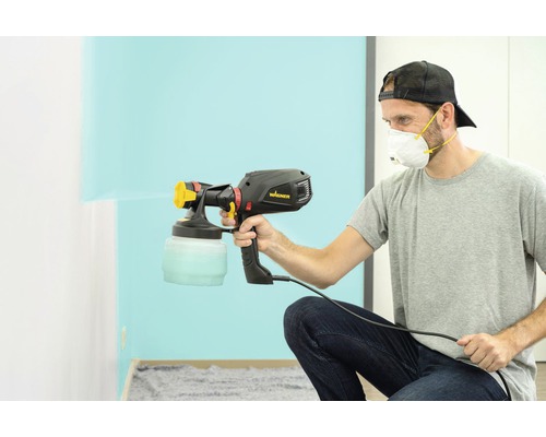 En man använder en Wagner färgspruta för att måla en vägg.