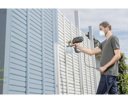 Man målar ett staket med en färgspruta.