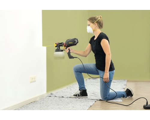 Kvinna använder en färgspruta för att måla en vägg.