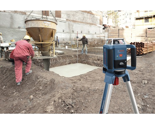 Rotationslaser på byggarbetsplats med betongarbeten och byggnadsarbetare