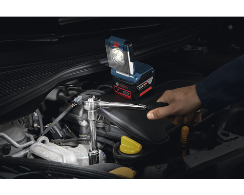 Batteridriven arbetslampa som används på en bilmotor med en hantverkare som använder en skiftnyckel