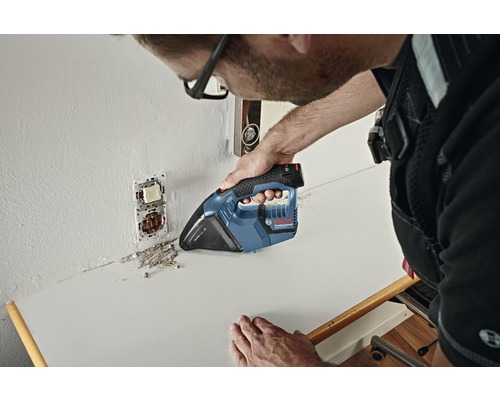 Hantverkare dammsuger byggdamm på en arbetsbänk med en batteridriven handdammsugare.