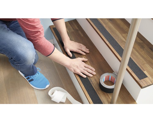 Person fäster halkskyddsremsor på en trätrappa.