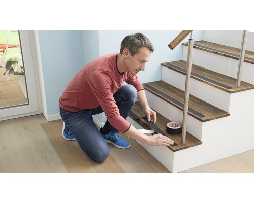 Man applicerar halkskyddstejp på en trätrappa. Rulle med halkskyddstejp synlig.