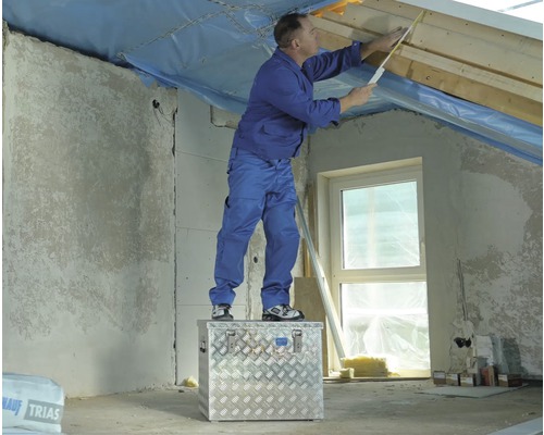 En man står på en verktygslåda och mäter en vind med en tumstock.