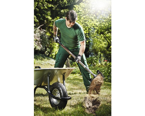 Man gräver med en spade i en trädgård bredvid en skottkärra.