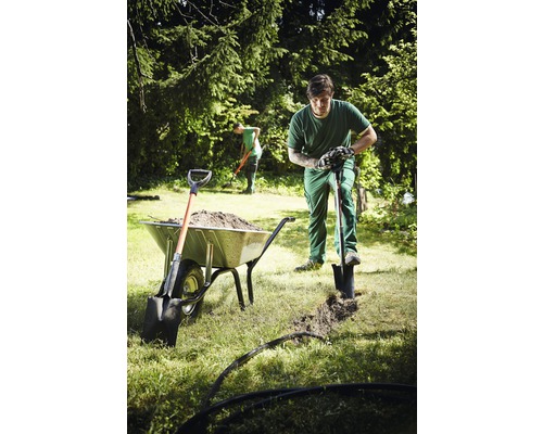 Trädgårdsmästare gräver ett dike med en spade bredvid en skottkärra full med jord.