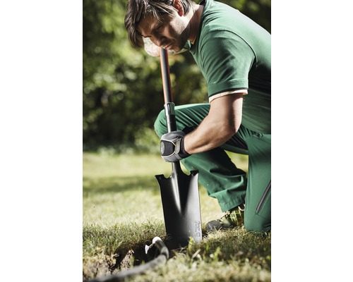 En man knäböjer i trädgården och gräver ett hål med en spade.