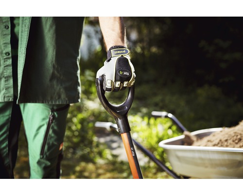 Trädgårdsmästare håller spade med handskar, skottkärra i bakgrunden