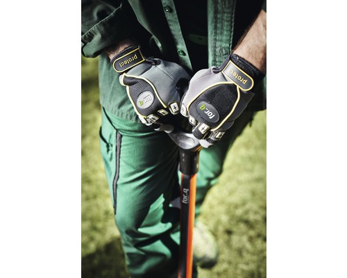 En person i arbetskläder håller en spade med trädgårdshandskar.