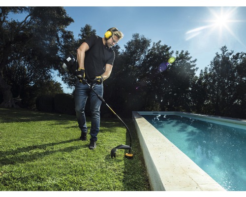 Man trimmar gräs med en grästrimmer nära en pool.