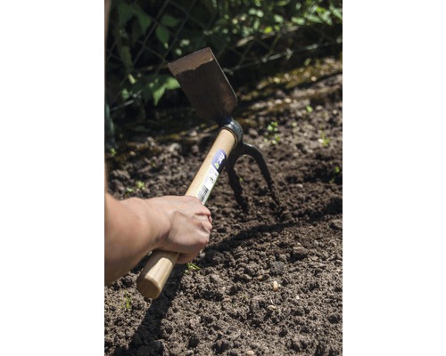 Hand håller en dubbelfunktionshacka i trädgårdsjorden