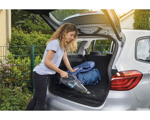 Kvinna dammsuger bagageutrymmet med en sladdlös handdammsugare