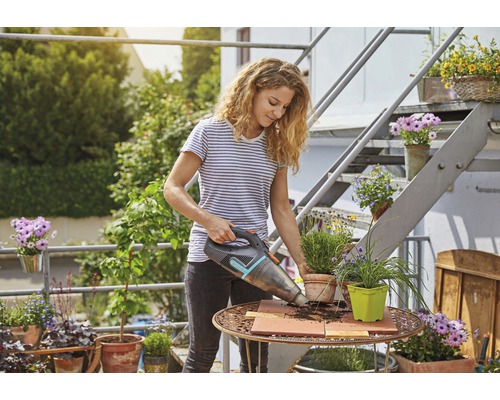 Kvinna dammsuger jord från ett trädgårdsbord med en sladdlös handdammsugare.
