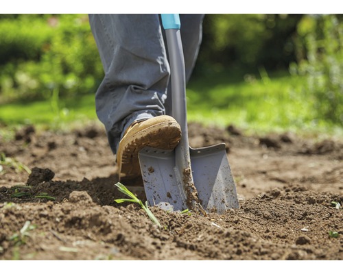 Person sticker spade i trädgårdsjord