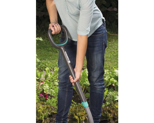 En person använder en spade i trädgården.