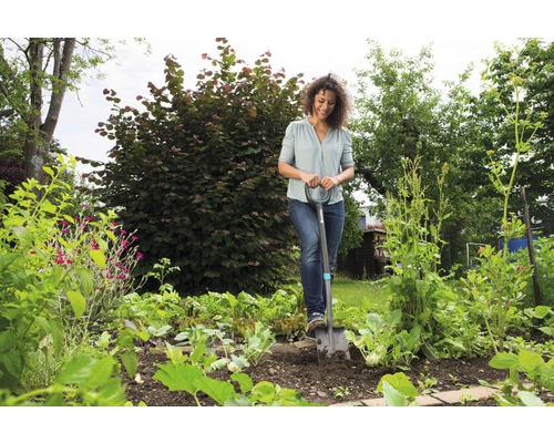 Kvinna använder spade i grönsaksträdgården.