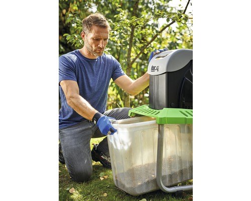 En man tömmer en behållare från en trädgårdshackare i en trädgård.