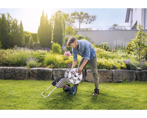 Man lindar upp trädgårdsslang på slangvagn i trädgården