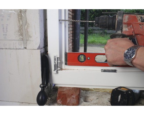 Ett fönster installeras med en borrmaskin och ett vattenpass.