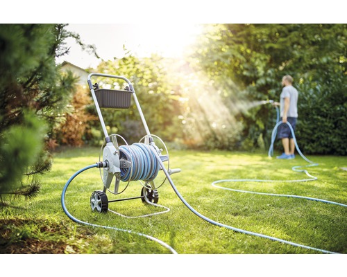 Trädgårdsscen med slangvagn och person som vattnar gräsmattan