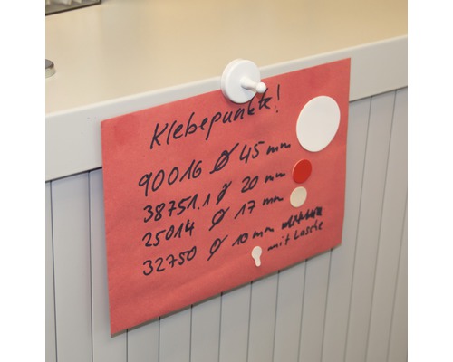 Ett rött pappersark med information om självhäftande prickar, fäst med en vit magnet.