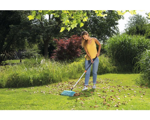 Kvinna sopar löv med en räfsa i trädgården.