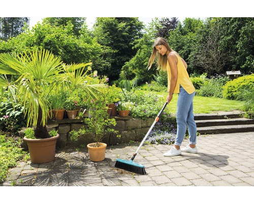 Kvinna som sopar stenterass med en gatukvast i en trädgård