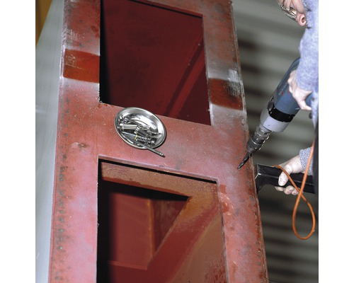 En person borrar i ett metallhölje med en borrmaskin. En skål med skruvar ligger bredvid.