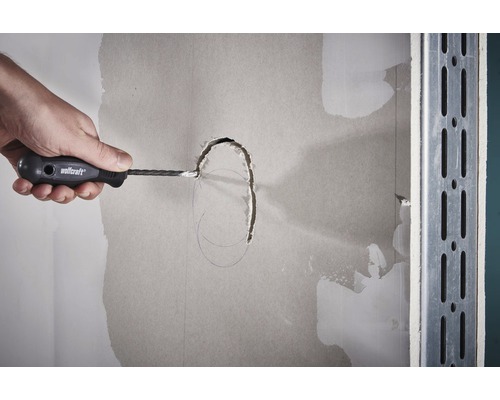 Hand skär ett hål i en gipsskiva med en gipsskiveskärare.