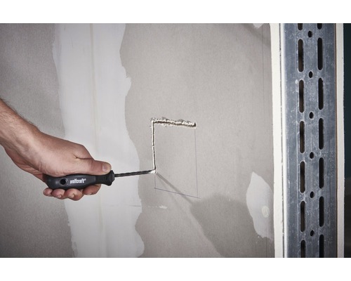 En person skär ett hål i en gipsskivavägg med en skärkniv.