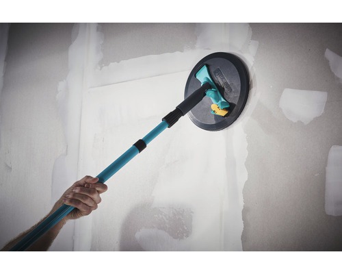 En person använder en takslipmaskin med teleskophandtag på en vägg.