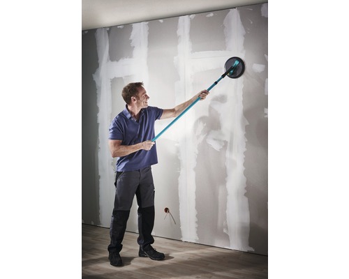 En man slipar en vägg med en slipmaskin med lång hals