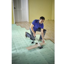 En man installerar laminat med ett dragjärn och stegljudsisolering i ett rum.