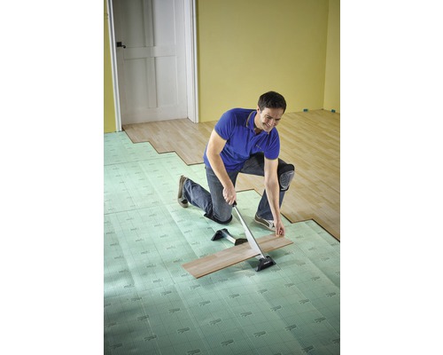 En man installerar laminat med ett dragjärn och stegljudsisolering i ett rum.