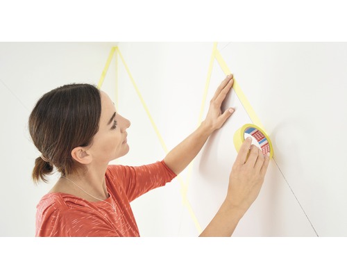 Kvinna applicerar maskeringstejp på en vägg för dekorativ målning