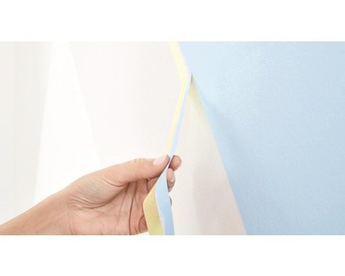 En hand drar bort maskeringstejp från en vägg