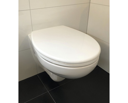 Vägghängd toalett med stängt toalettlock framför en kakelvägg