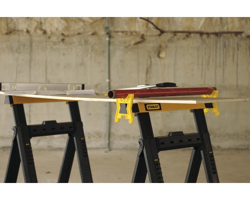 Två arbetsbockar med träskiva, vattenpass och verktyg. Stanley logotyp.