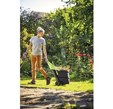 Kvinna drar en trädgårdsvagn full med löv genom trädgården.
