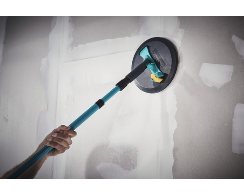 En person jämnar ut en vägg med en takslipmaskin med teleskophandtag.