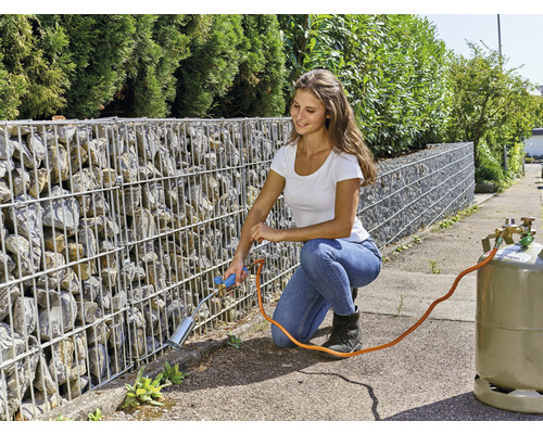 Kvinna tar bort ogräs med en gasbrännare mot en gabionmur