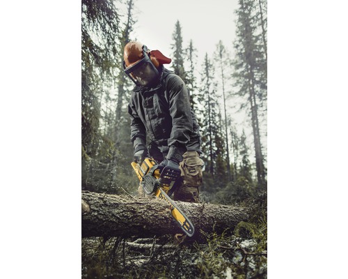 Man med skyddskläder och motorsåg som sågar ved i skogen