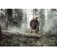 En man med skyddsutrustning sågar en trädstam med en motorsåg i en skog.