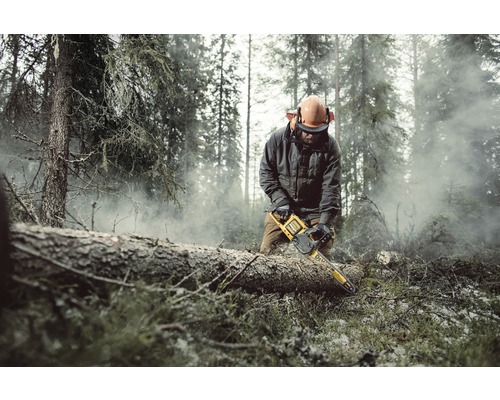 En man med skyddsutrustning sågar en trädstam med en motorsåg i en skog.