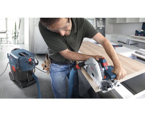 Hantverkare arbetar med en sänksåg på en träskiva, ansluten till en industridammsugare från Bosch.