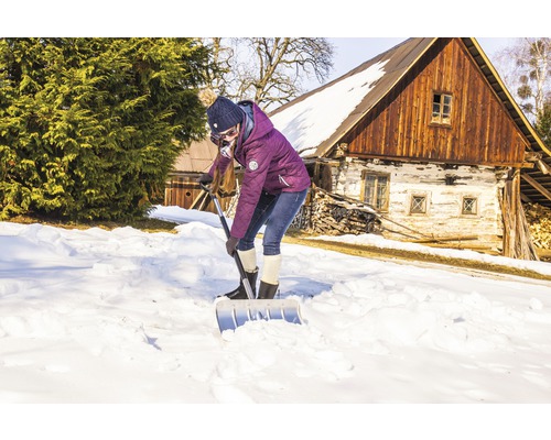 Kvinna skottar snö med en snöskyffel framför ett hus.